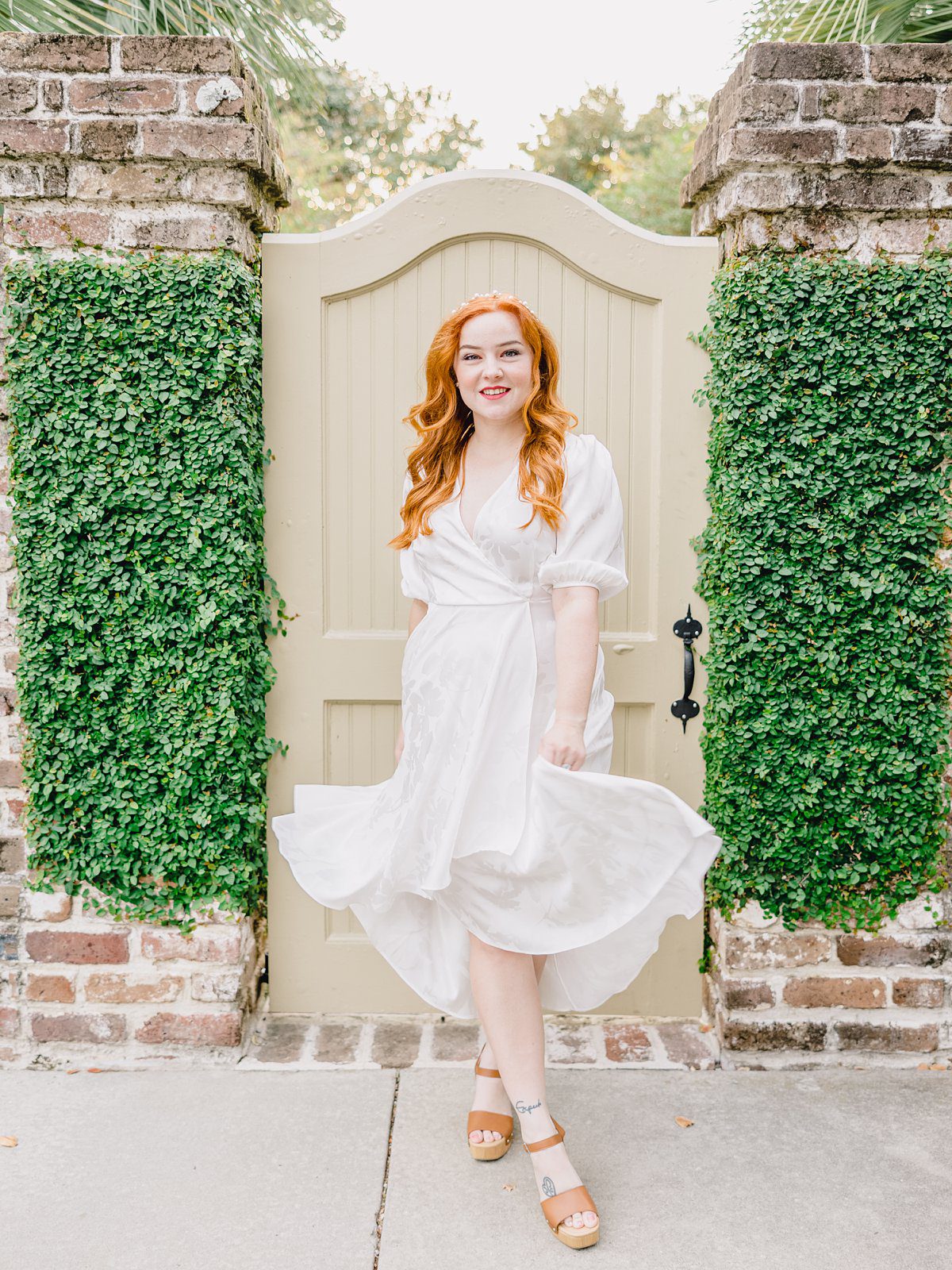 red haired woman in white flowy dress in front of a white gate downtown