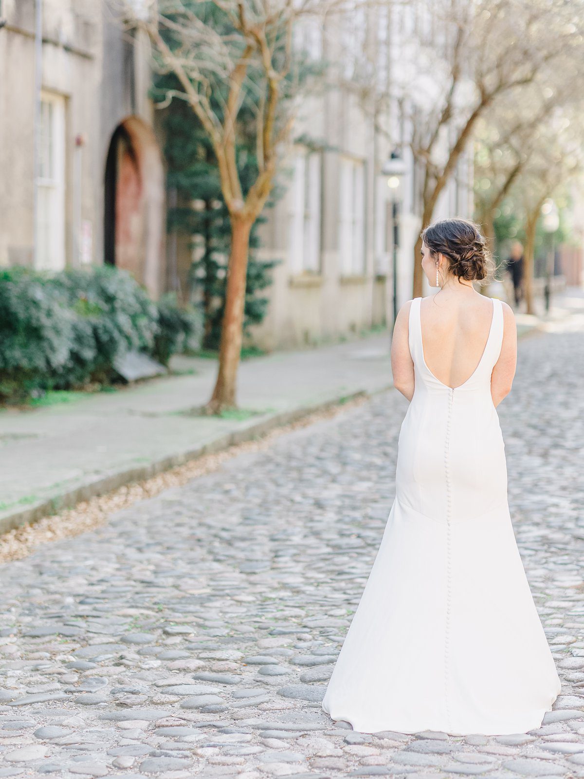 bride in simple white gown in downtown Charleston on cobblestone street