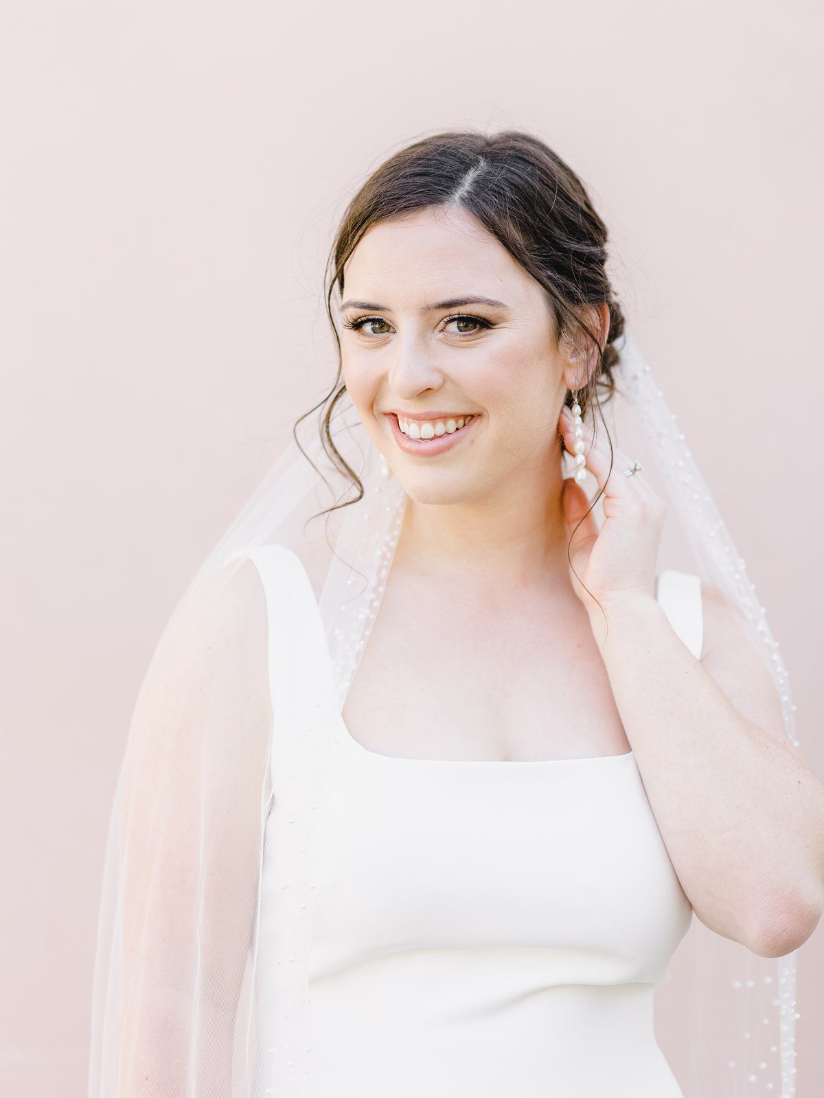 bride in simple white gown in front of a pink wall in downtown Charleston at her bridal session