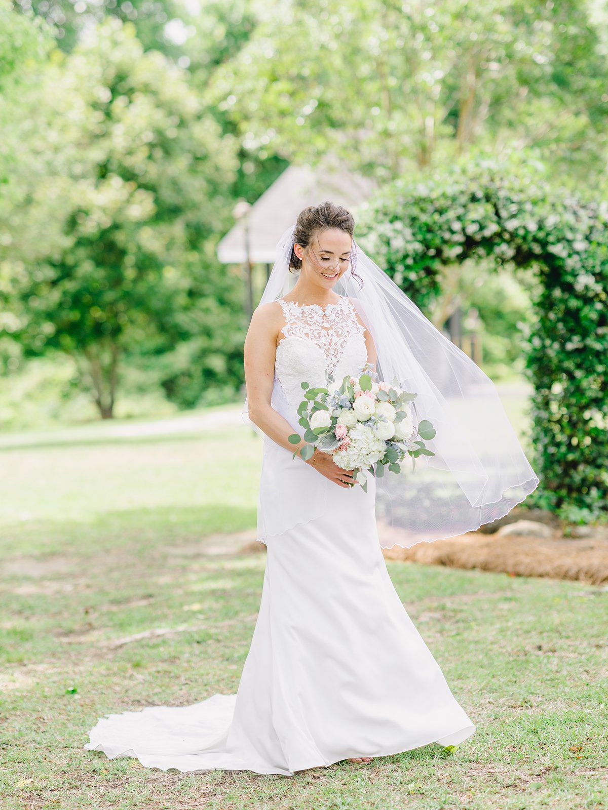 bridal portrait in green grass surrounded by trees as the breeze blows