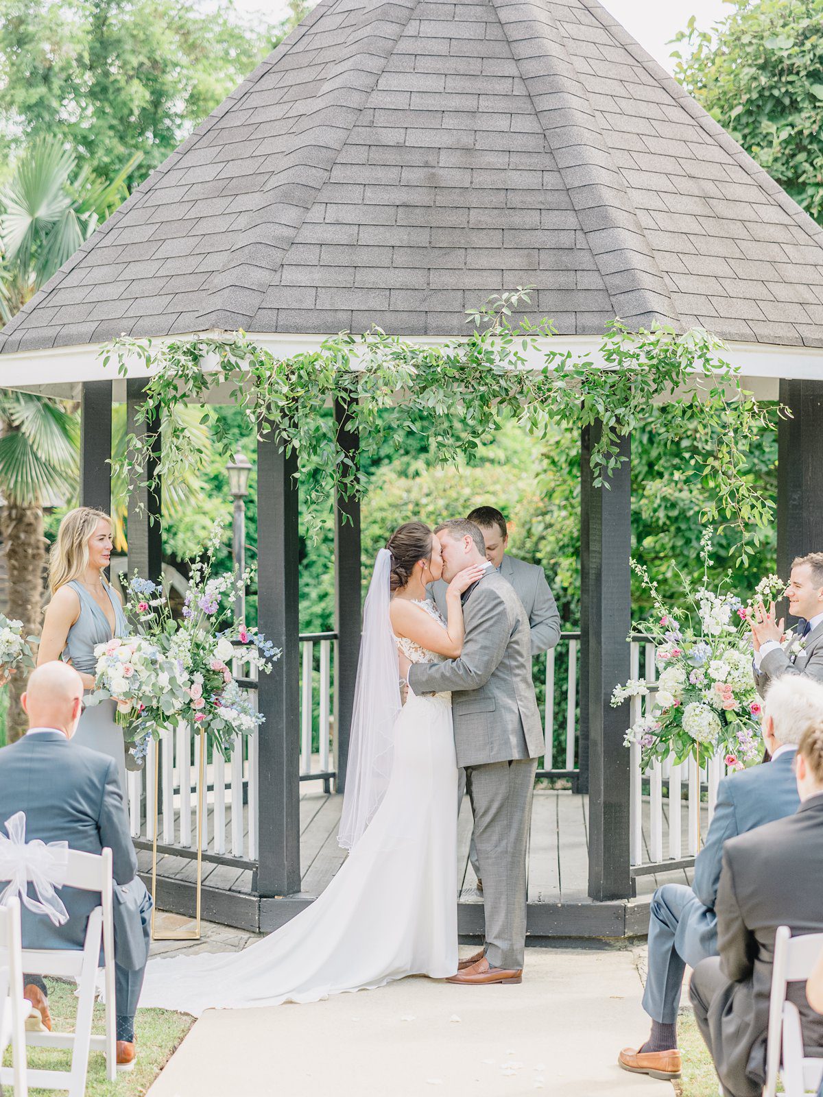 couple shares a first kiss as newlyweds surrounded by greenery and pink and blue flowers