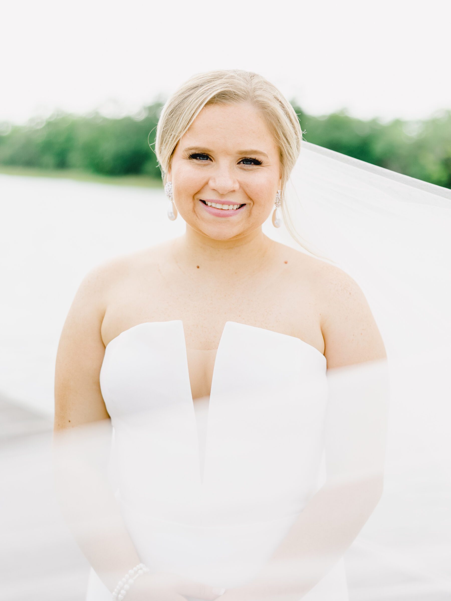 A beautiful, smiling bride with her veil flowing in the breeze at her Citadel docks bridal session