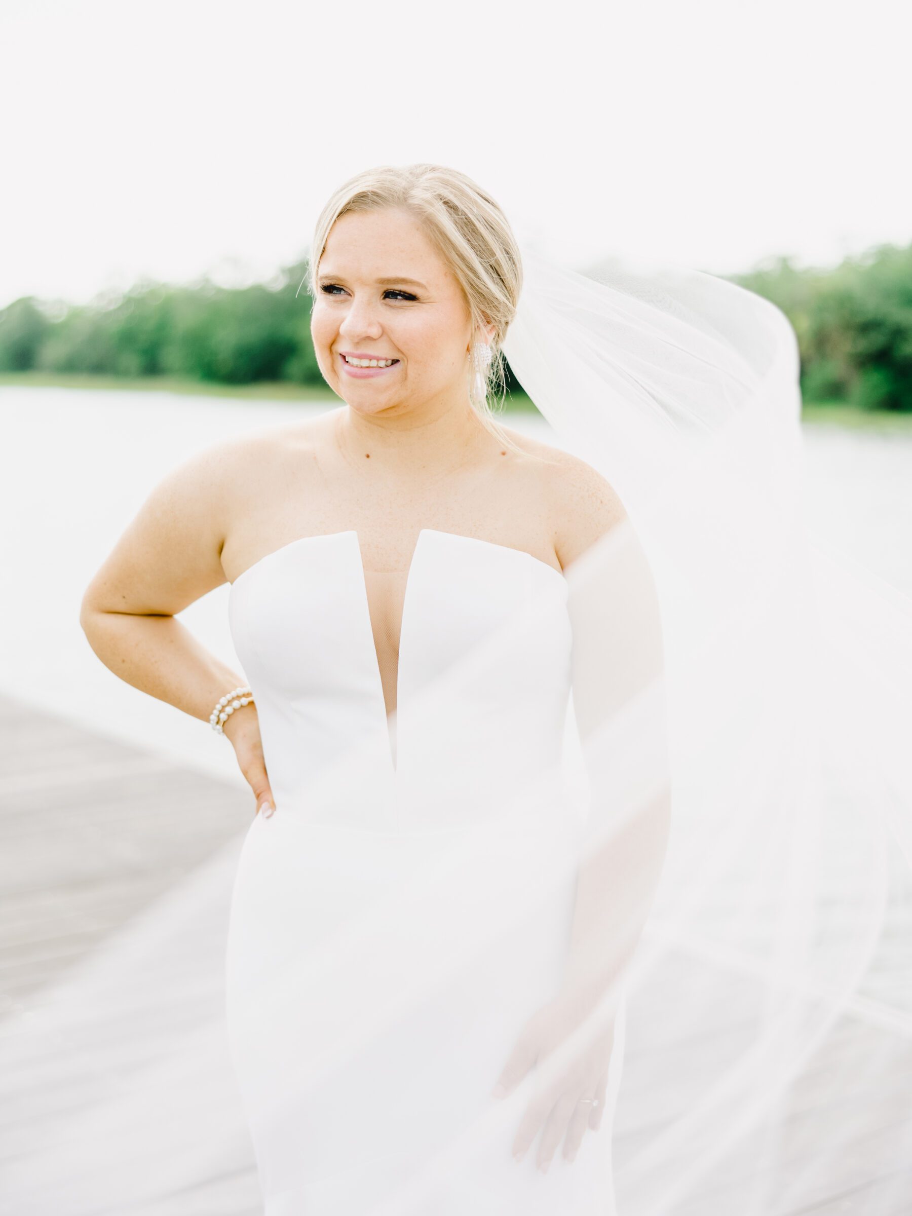 A beautiful, smiling bride with her veil flowing in the breeze at her Citadel docks bridal session