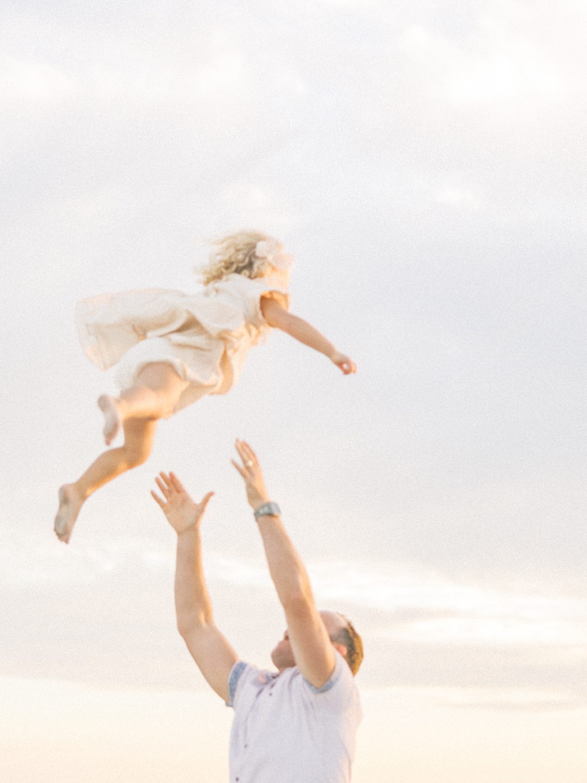 dad tosses little girl in the air at beach family session
