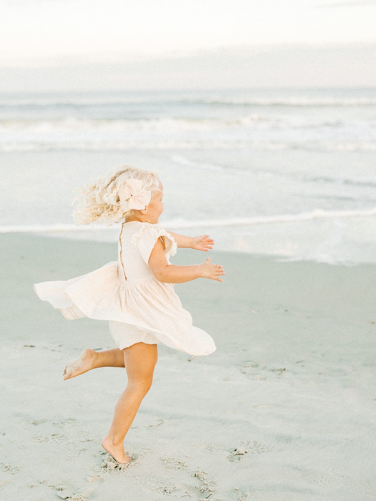 little girl spins on the beach with bow in her hair