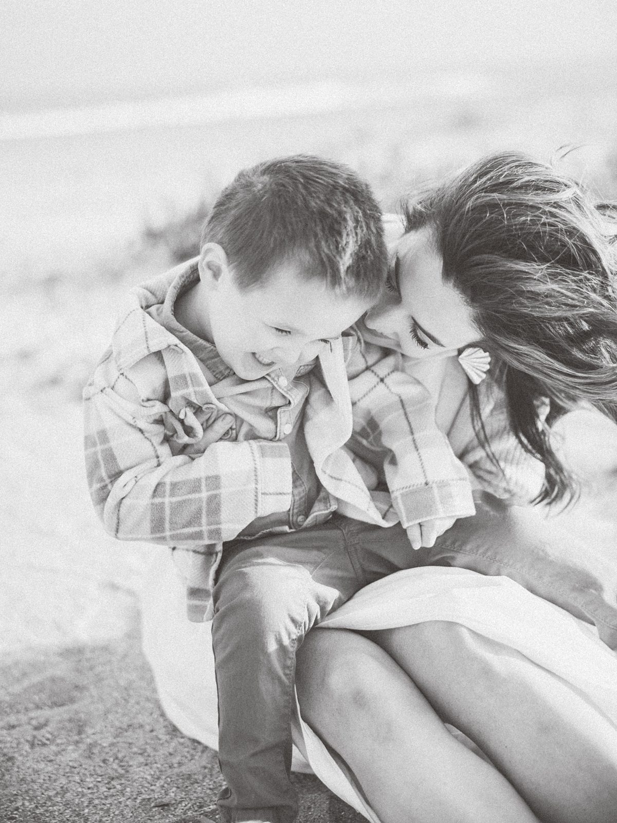 mother tickles son in the sand at the beach