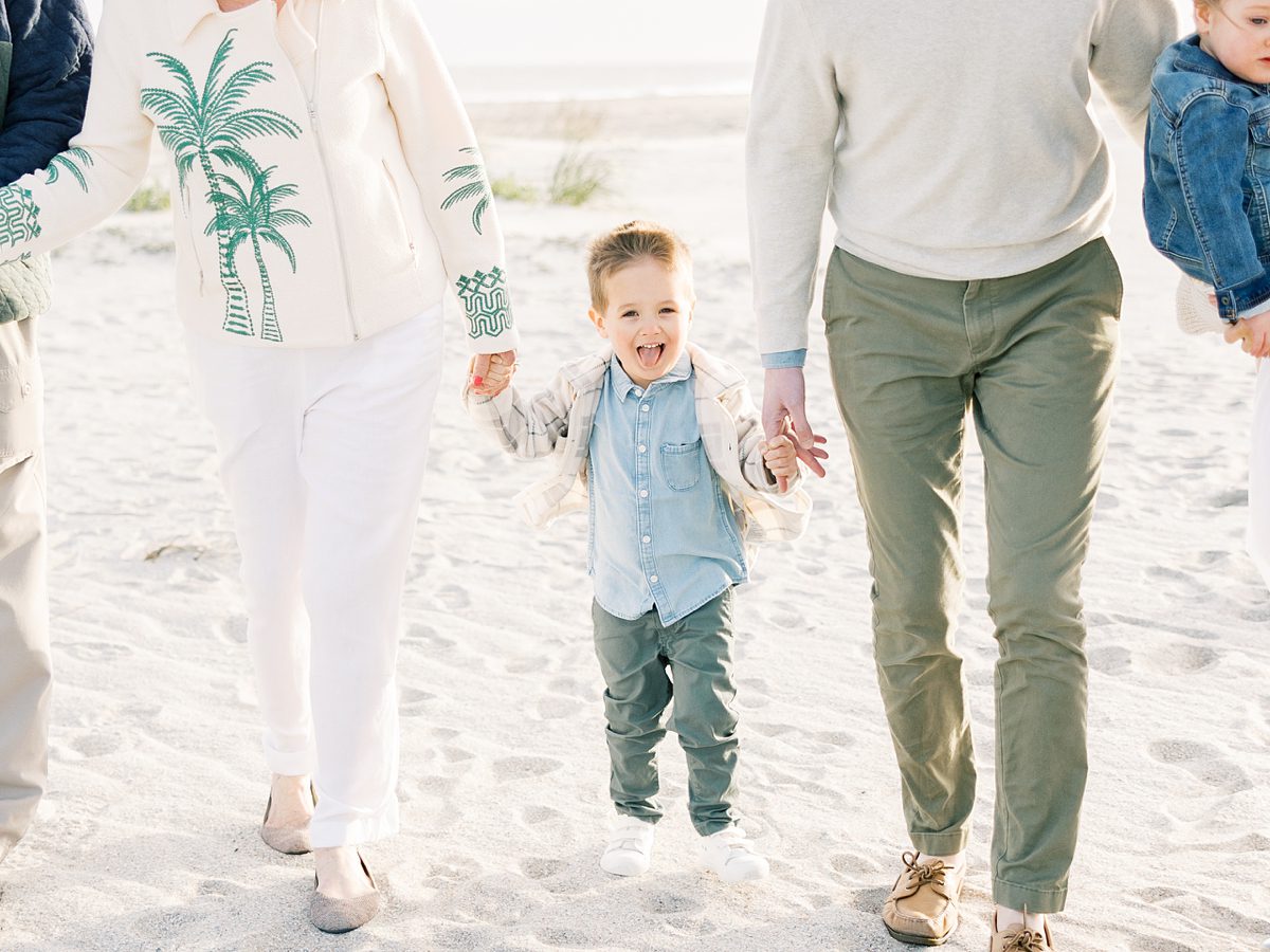 little boy holds his parents hand on the beach