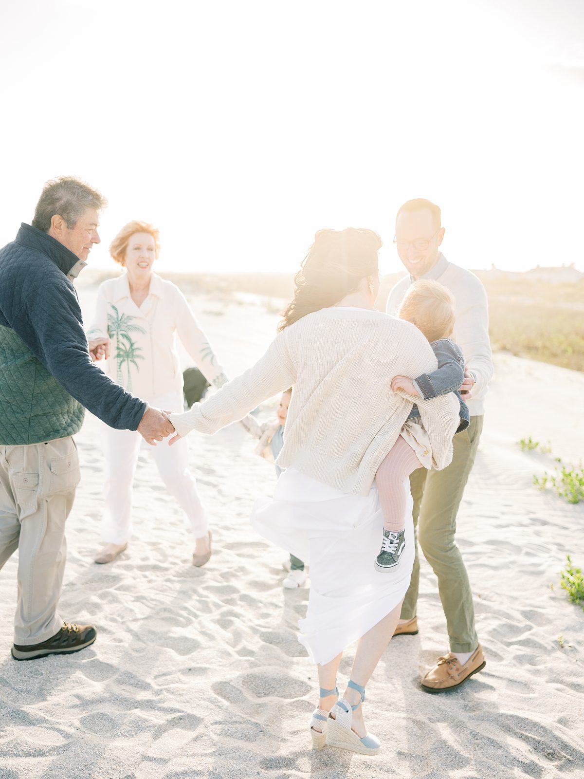 family plays ring around the rosie on the beach at sunset