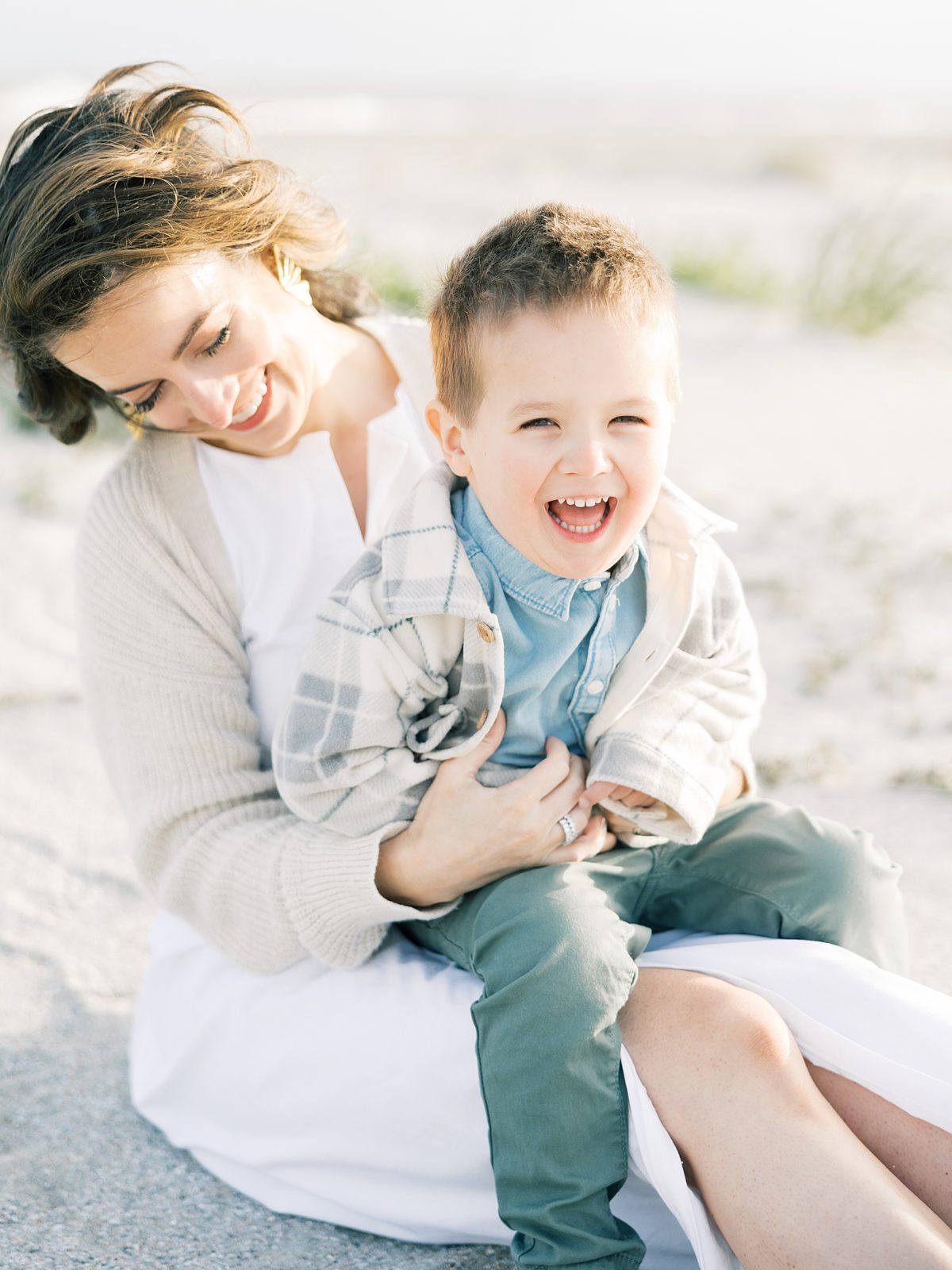 mom tickles son sitting in the sand