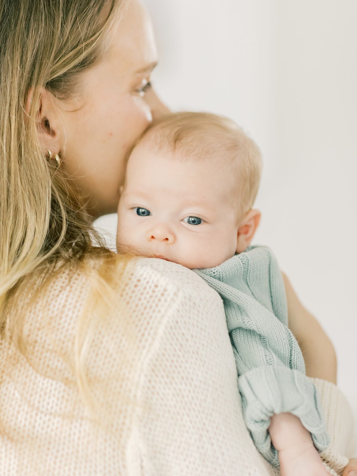 baby girl peeks over mom's shoulder with big blue eyes