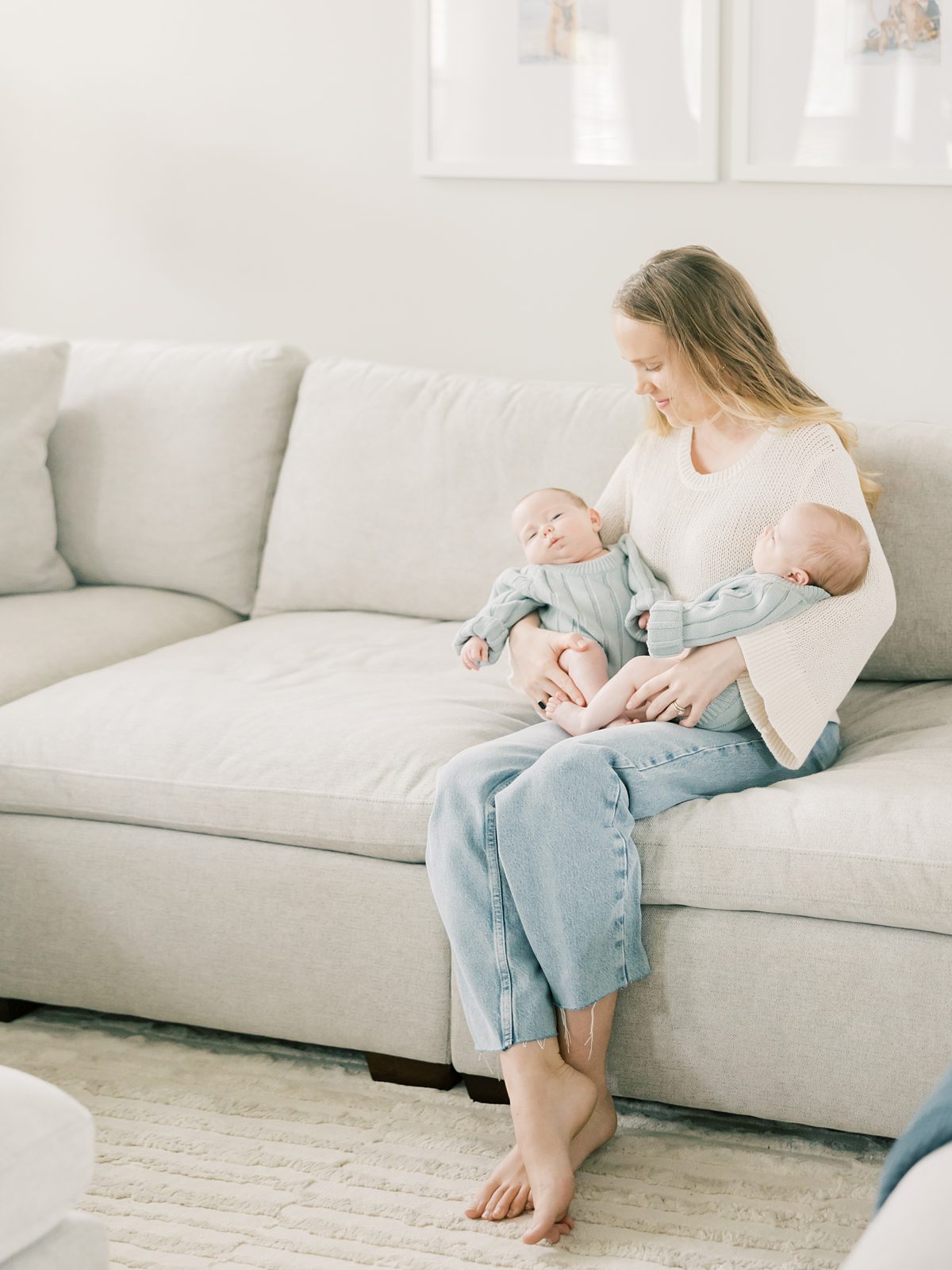 mom cradles twin newborn girls on the sofa at their in-home newborn session