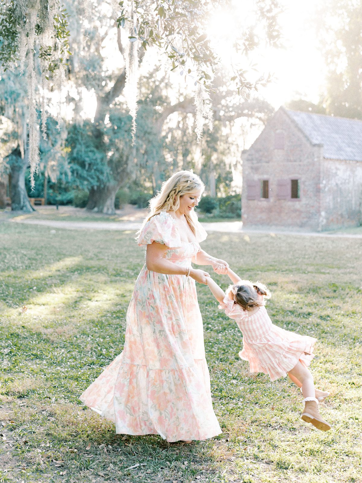 mom in floral dress swings around daughter in pink dress